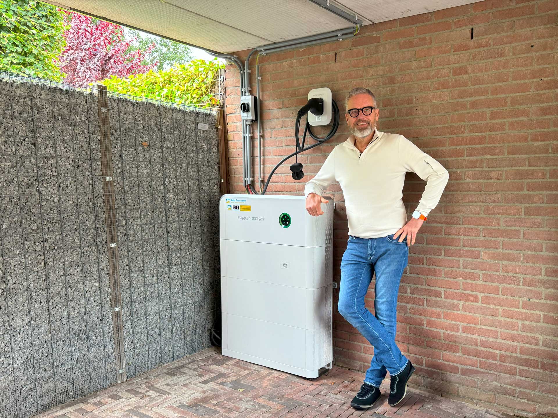 Tevreden klant (man) staat  bij een thuisbatterij van Sigenergy onder de carport